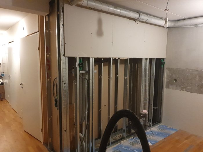 Renovering pågår, metallstomme exponerad, installationsrör synliga, ofärdiga väggar, ledningar, byggarbetsplats inomhus.