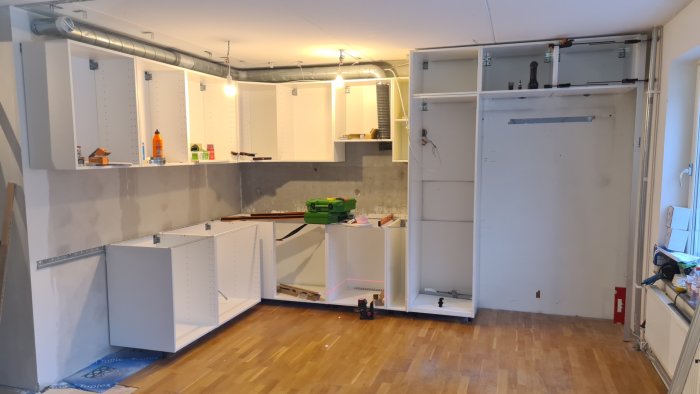 Ett kök under renovering med osammanhängande skåp och exponerad rörledning.