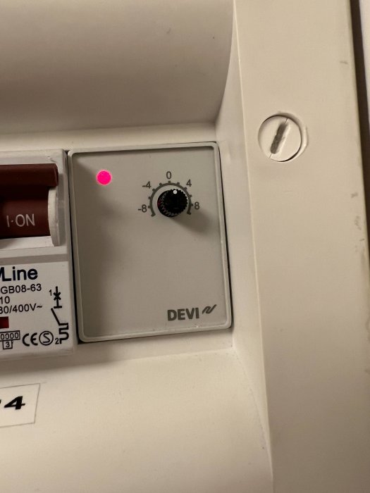 Reglagepanel med ratt, röd lysdiod, vit bakgrund, elektrisk enhet märkt "DEVI", skala -8 till +8.