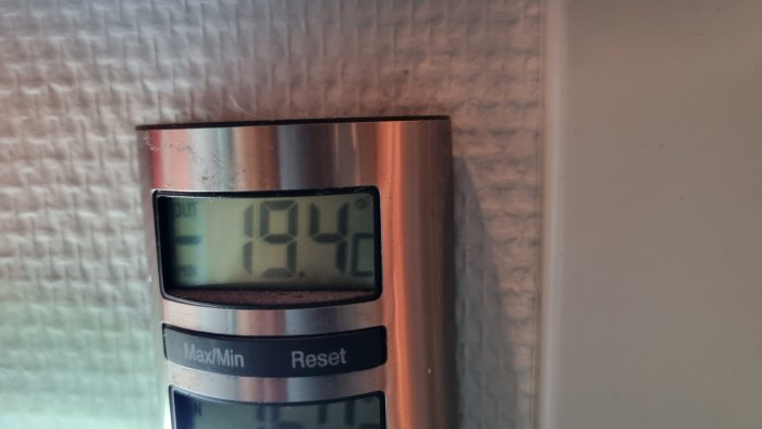 Digital termometer visar inomhustemperatur 19.4°C mot en texturerad väggbakgrund.