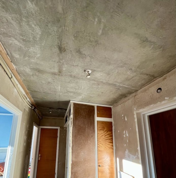 Renoveringsarbete pågår, oslipade väggar, tak utan färdig yta, spackel, byggmaterial synligt, ofärdigt rum.