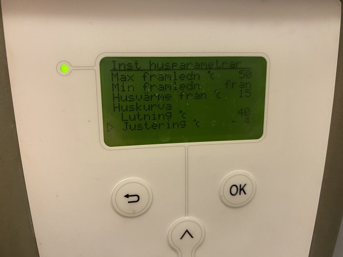 Digital display på värmeregleringssystem med knappar för navigering och inställningar. Text på svenska och grönt ljus indikerar drift.