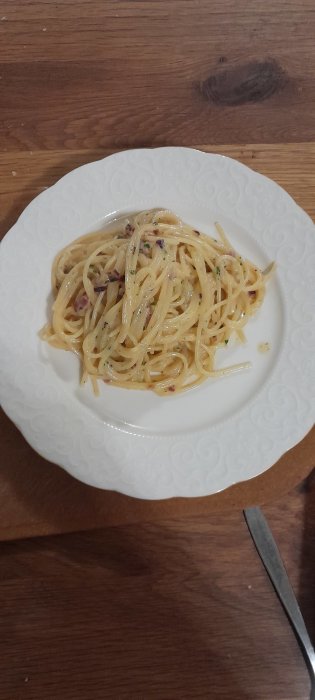 En tallrik med spaghetti carbonara på ett träbord, nära en kniv. Enkel, hemlagad måltid.