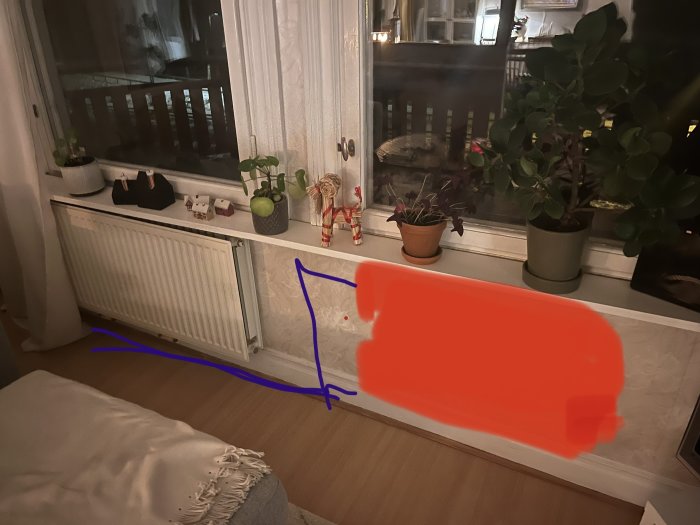 Ett vardagsrum med fönster, element, växter, dekorationer och en soffa. En del är övermålad med rött.