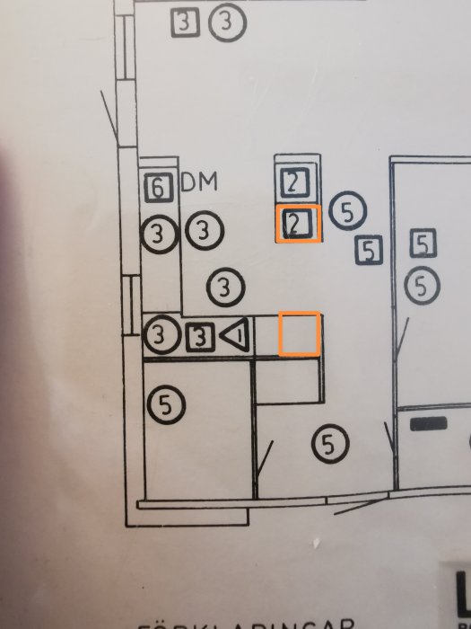 Del av en planritning, markerad med orange, möbleringssymboler, nummer och bokstäver.