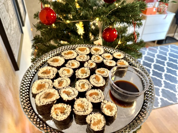 Ett fat med sushi och sojasås, framför ett juldekorerat rum.