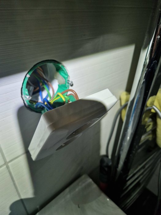 Öppen eluttagsinstallation, kablar synliga, väggplatta hänger lös, inomhusmiljö, säkerhetsrisk, reparation behövs.