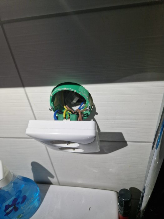 Öppen handtork med inre elektronik synlig, monterad på en vägg, ovanför tvåltillbehör och flaska.