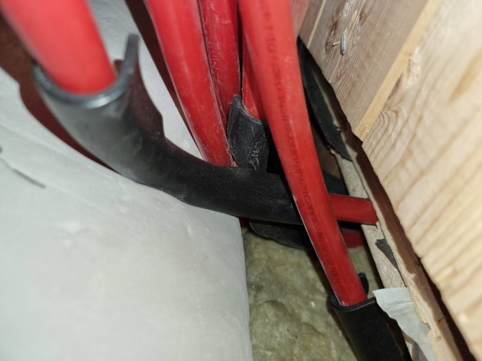 VVS-installation, röda rör och svart slang i trångt utrymme, isolering synlig.
