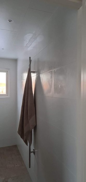 Modernt badrum med kaklade väggar, handduk på stång, spotlights i tak, och mjukt naturljus.