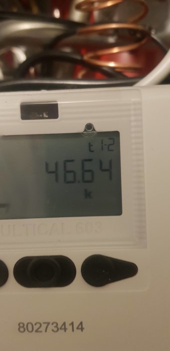 Digital display visar 46.64 och texten "MULTICAL 603". Ser ut som en energi- eller vattenmätare. Oskarpt bakgrund, möjligtvis kök.