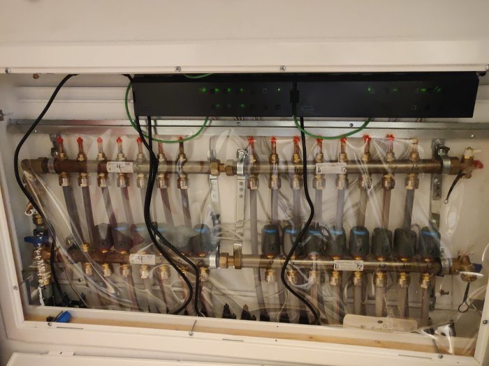 Uppvärmningssystem med rör, ventiler och en eldistributionenhet i ett tekniskt skåp.