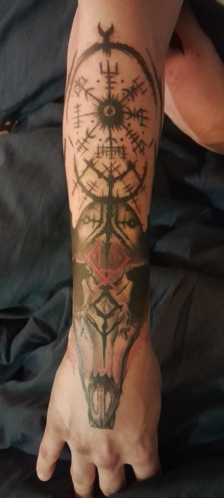 En persons arm med detaljerad svart underarms-tatuering, kreativ design, symboler, mönster och en djurform.