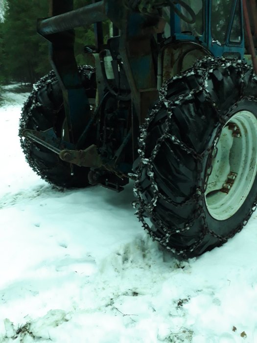 Traktordäck med kedjor på snötäckt mark. Skogsmiljö. Winter traction aid for vehicle.