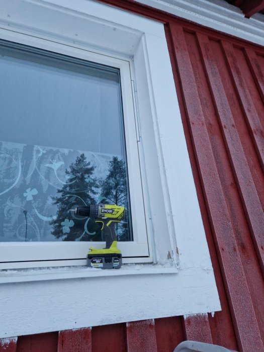 Fönster med blomdekor, verktyg (skruvdragare) på fönsterbräda, röd trävägg, vit kant, utomhus.