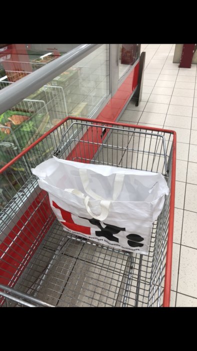 En shoppingvagn med en plastpåse inuti, vid frysdisken i en butik.