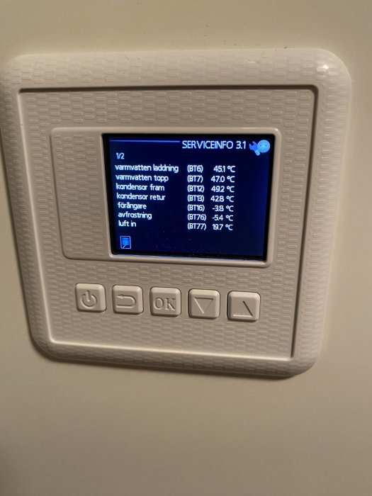 Digital display visar temperaturer för olika komponenter i ett värmesystem, omgivet av knappar på en vit panel.