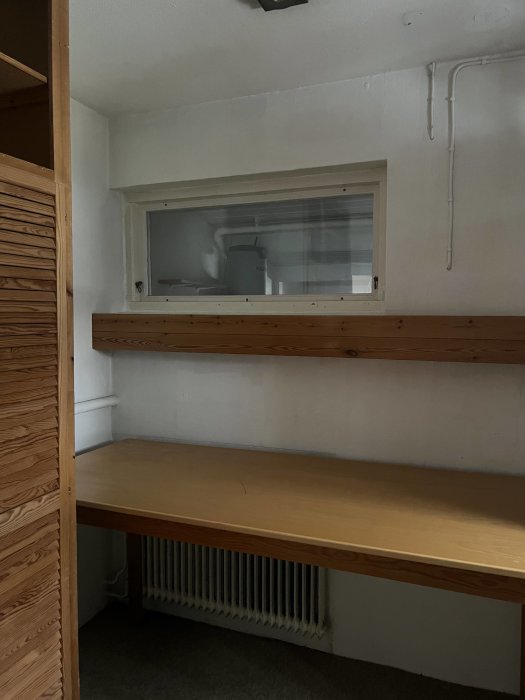 Ett tomt arbetsrum med träskrivbord, hyllor och ett litet fönster med utsikt mot en datorstol.