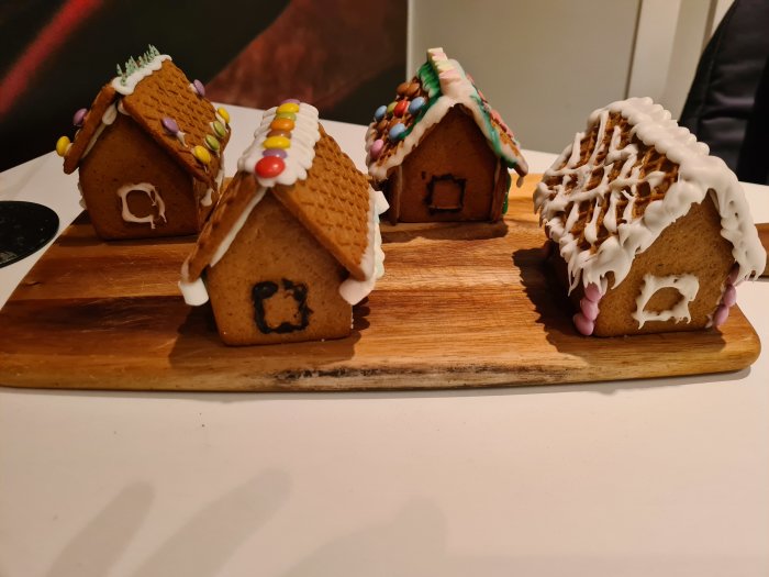 Tre pepparkakshus dekorerade med frosting och godis på en träskärbräda.