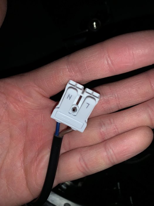 En hand håller en vit plastkontakt med en ansluten svart kabel.