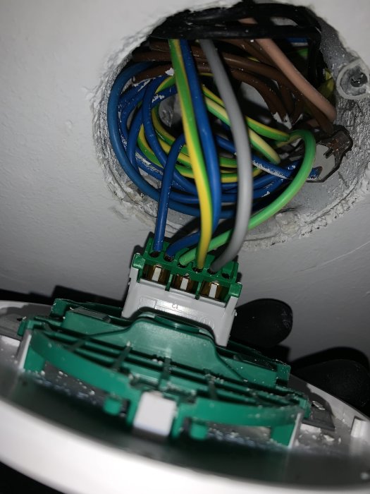 Närbild av öppnat eluttag med flera färgade elkablar och kopplingsklämma, vägginstallation, ej färdigställd.