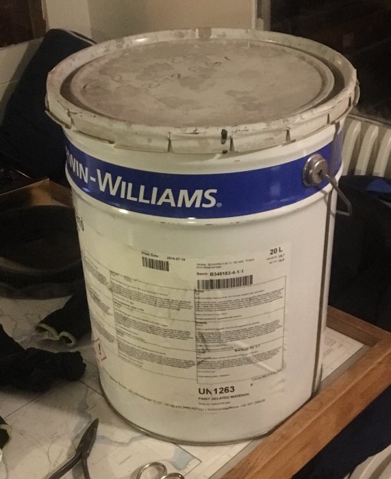 En 20-liters vit färgburk från Sherwin-Williams står på golvet intill saker.