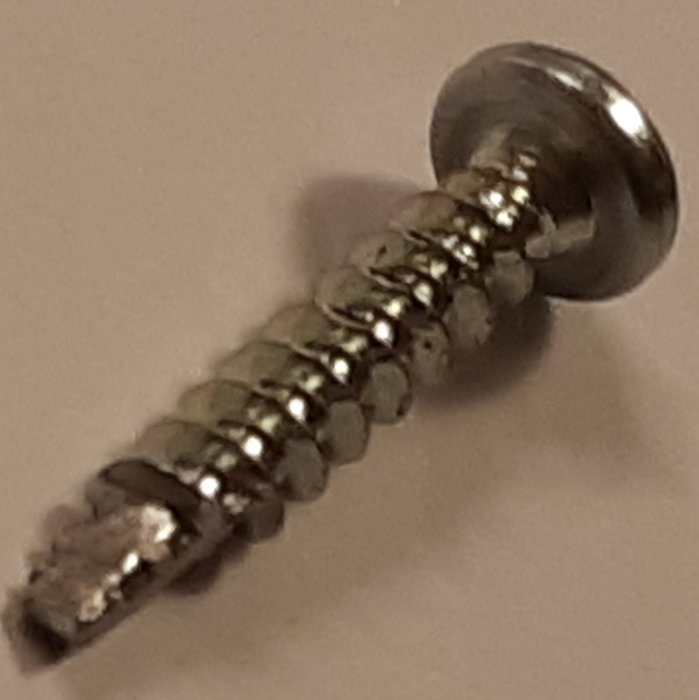 En metallschraub med rundat huvud och gängor synlig mot suddig vit bakgrund.