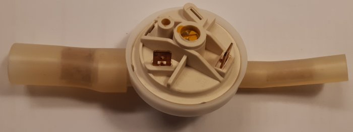 Ett vitt plastföremål, troligen en del av en apparat, med sladdar och elektroniska komponenter synliga.