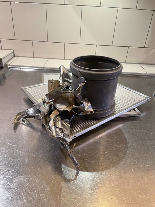 En förstörd kruka ligger på en ugnsgaller som är placerat på ett rostfritt stålbord mot vita kakelplattor.