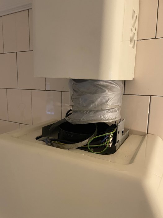 En demonterad köksfläkt på en diskbänk, synliga elektriska anslutningar, vita kakelväggar.