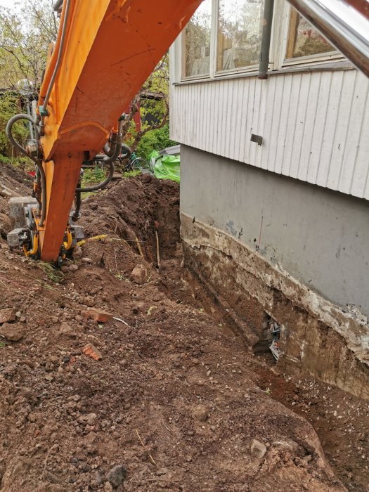 Grävmaskin nära husgrund, gräver, jord och grus, delvis avtäckt grund, arbetsplats, uteområde.