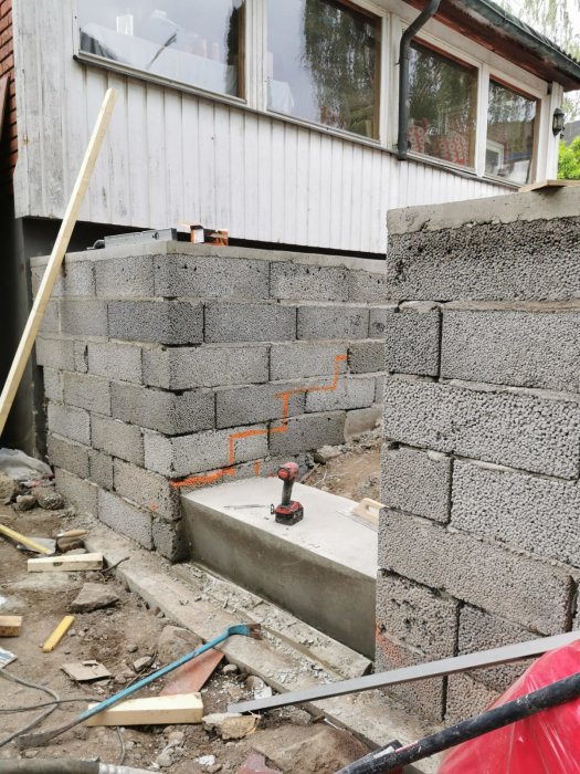 Byggarbetsplats med gråa betongblock, verktyg utspridda, byggnad under konstruktion, oordning, dagtid.