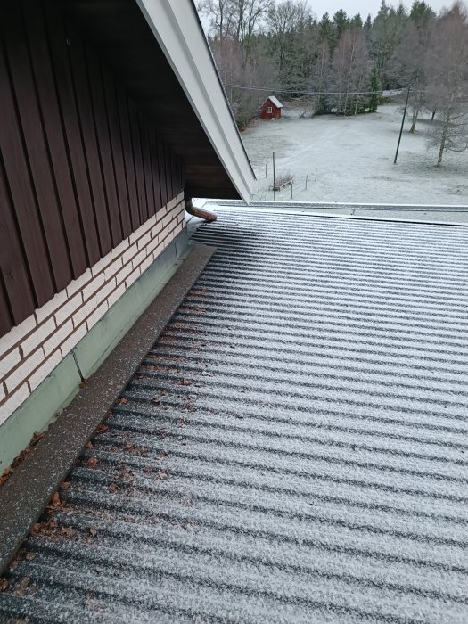 Takränna, tegelvägg, snötäckt plåttak med löv, träd, rött hus, disigt landskap, tidig vinter eller sen höst.