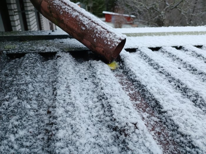 Ett snötäckt hustak med en brun takränna och synliga takpannor.