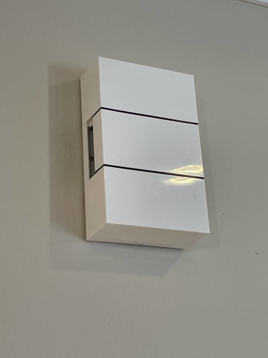 Vit, modern vägglampa med reflektion och skugga på en ljus vägg.