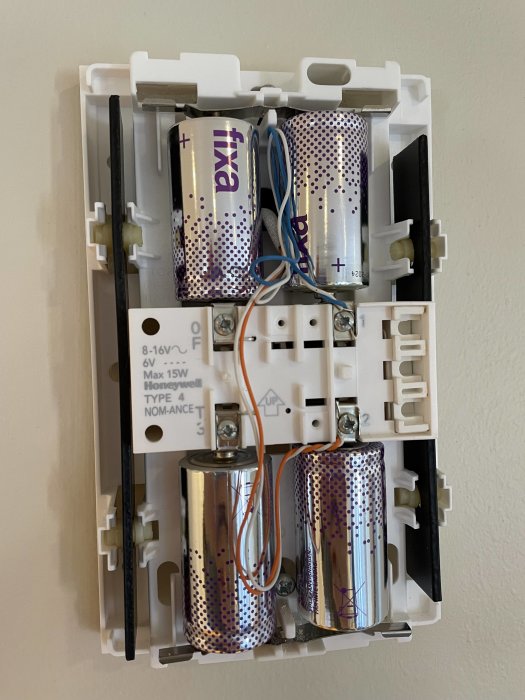 Öppen värmetermostat med synliga batterier och ledningar, väggmonterad, elektrisk innerkomponent, mekanisk uppbyggnad.