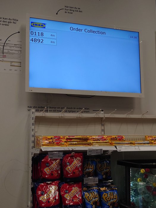 En skärm visar "Order Collection" ovanför godishyllor i en butiksmiljö.