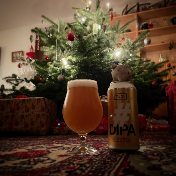 Ölglas och burk framför julgran med dekorationer och presenter. Mysig, festlig atmosfär.
