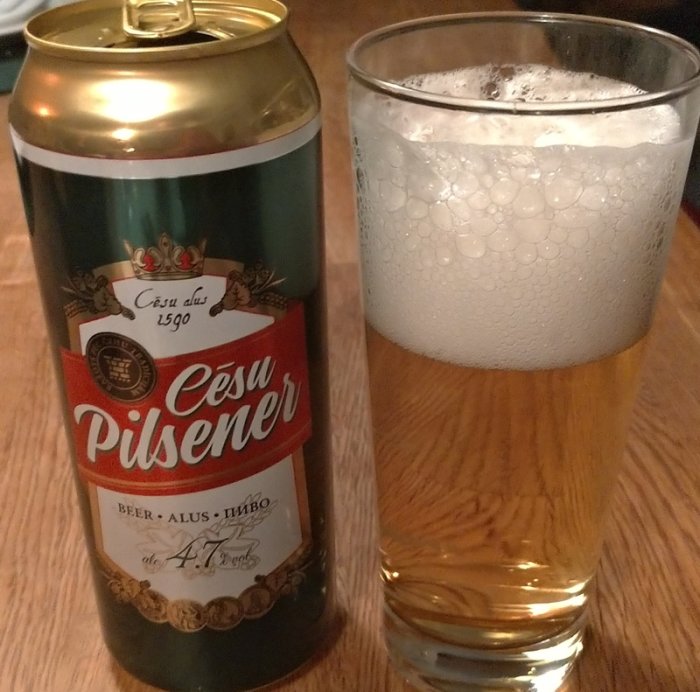 Ölburk med texten "Cēsu Pilsener" bredvid ett glas fyllt med öl och skum.