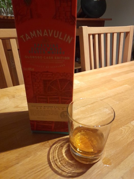 Flaska och glas med whisky, träbord, stol i bakgrunden, inomhus, mysig belysning. Tamnavulin, Speyside Single Malt Scotch.