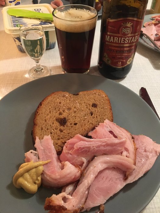 Skinka, senap, russinbröd på tallrik. Mariestads julöl, snaps, smörkniv och smörbytta i bakgrunden. Festlig måltid.