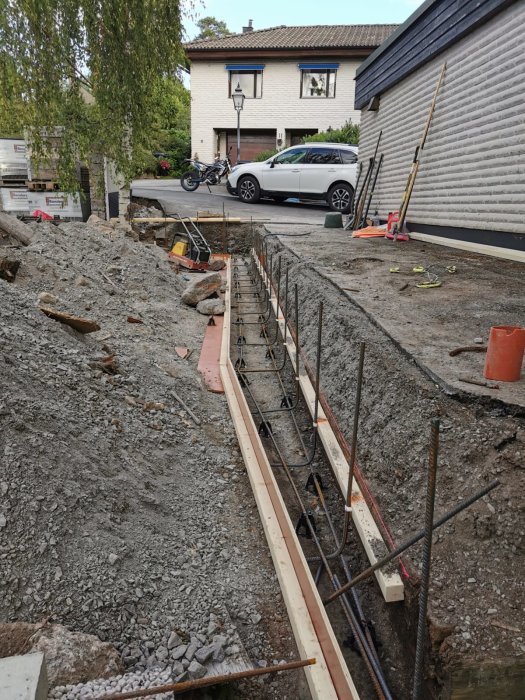 Grundarbete för betongplatta, armeringsjärn, hus, bil och motorcykel synliga i bostadsområde.