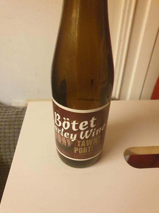 Brun glasflaska med etikett "Bötet Barley Wine Tawny Port" på vit yta.