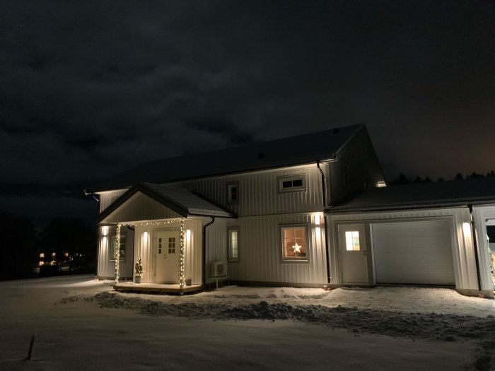 Ett hus med juldekorationer och belysning under en natt med snö.