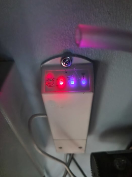 En elektronisk apparat med tre upplysta knappar och en optisk sensor monterad på en vägg.