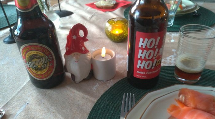 Ett julbord med ölflaskor, tända ljus, juldekoration i form av en tomtefigur och lax.