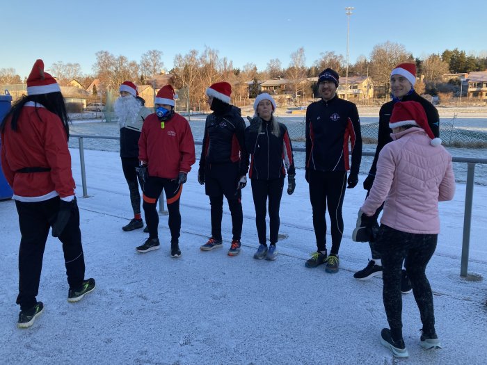 Grupp människor i sportkläder och tomtemössor står på snötäckt mark utomhus.