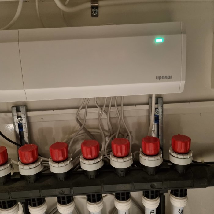 Värmefördelare för golvvärme med rör och reglerventiler under en elektronisk enhet från Uponor.