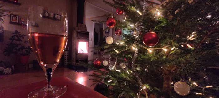 Mysig julstämning med glittrande gran, juldekorationer, eldstad och ett glas rosévin.