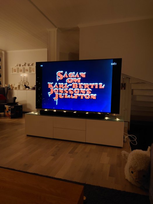 Ett vardagsrum med TV som visar titeln på en svensk julberättelse, inredning, parkettgolv, mjukdjur till höger.